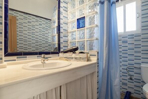 A bathroom with a white sink, a mirror, a blue shower curtain, and a tiled wall with a blue and white pattern. - Rural House 'Casas Pepe 1' with Private Terrace, Wi-Fi and Air Conditioning (Los Caños de Meca)