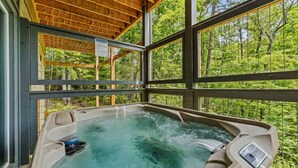 Een hottub met een houten plafond en grote ramen met uitzicht op een bos.