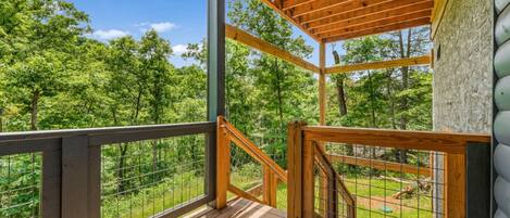 A wooden deck with a metal railing, overlooking a forested area.