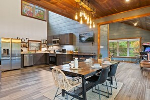 Una cocina moderna con electrodomésticos de acero inoxidable, un comedor con mesa y sillas de madera, y un amplio ventanal con vistas al exterior.