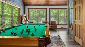Een pooltafel in een ruimte met houten plafond en grote ramen.