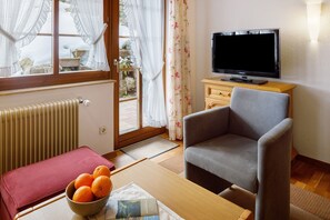 A living room with a sofa, a television, a radiator, a window with curtains, and a bowl of oranges on a table. - Apartment 'Tannenliebe' with Private Terrace, Shared Garden and Wi-Fi (Feldberg-Altglashütten)