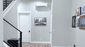 Un interior moderno con una escalera, un pasillo con suelo de madera, un aire acondicionado de pared y obras de arte enmarcadas.