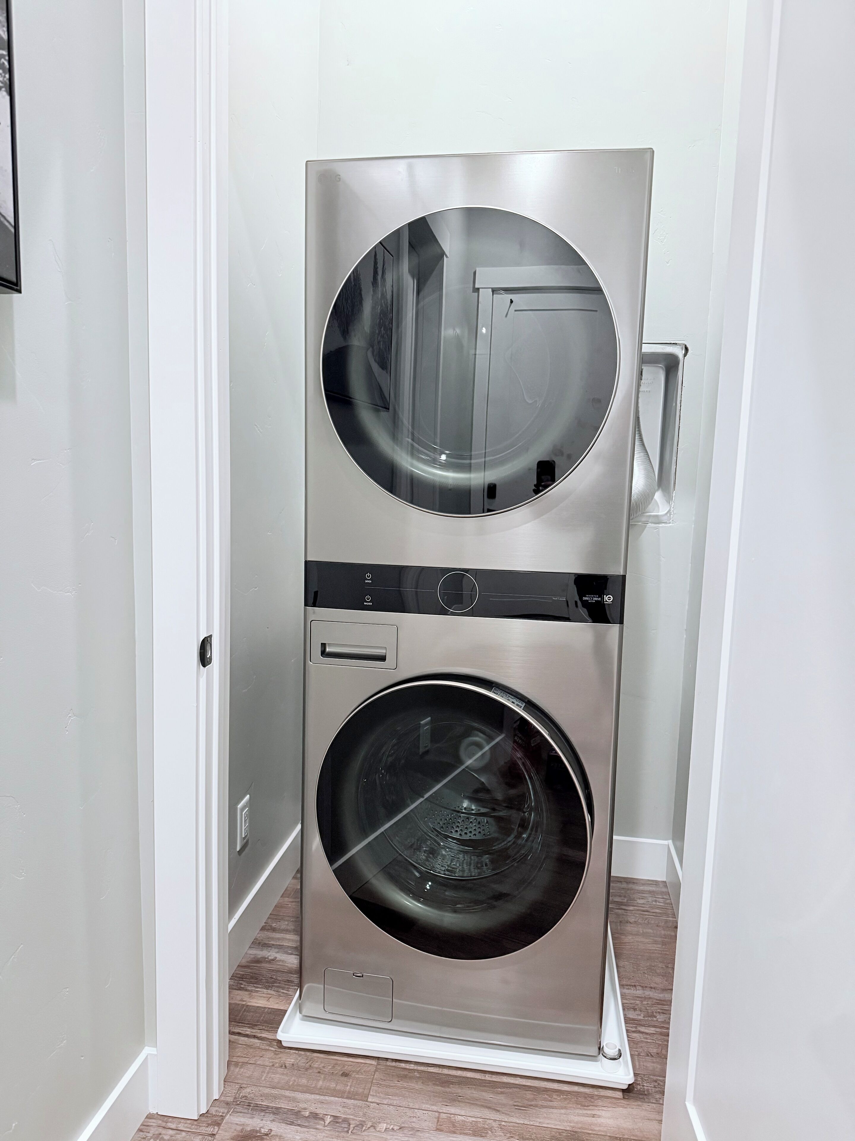 A compact, stainless steel wall-mounted washer and dryer unit with a control panel and a small storage compartment.