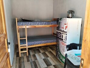 Ein Stockbett mit gemustertem Matratze, ein kleiner Kühlschrank und ein Tisch mit einer Tasche darauf.