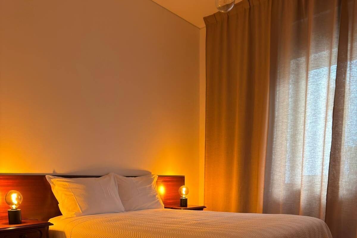 A neatly made bed with a white blanket, two bedside lamps, and a wooden nightstand.