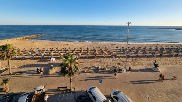 Una spiaggia con file di ombrelloni, un’area parcheggio e una statua.