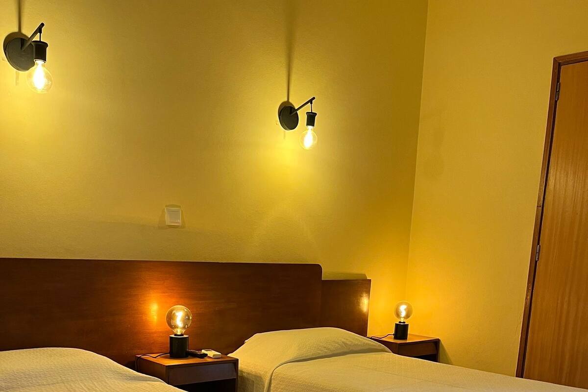A hotel room with two beds, each with a bedside lamp and a nightstand.