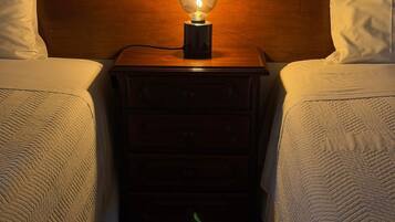 Habitación de hotel con dos camas, un cabecero de madera, una mesita de noche con lámpara y una luz verde en el suelo.