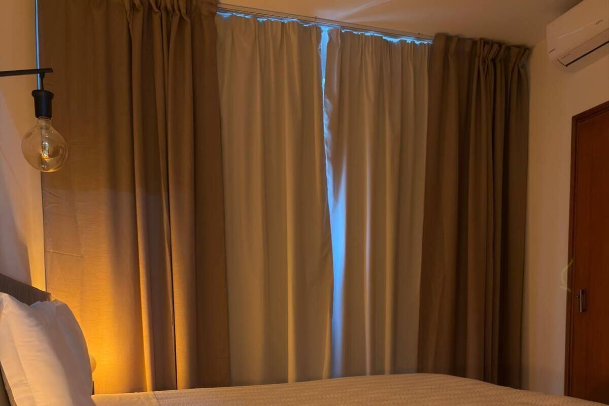 A bedroom with a bed, a bedside lamp, a wooden nightstand, and a window with curtains.