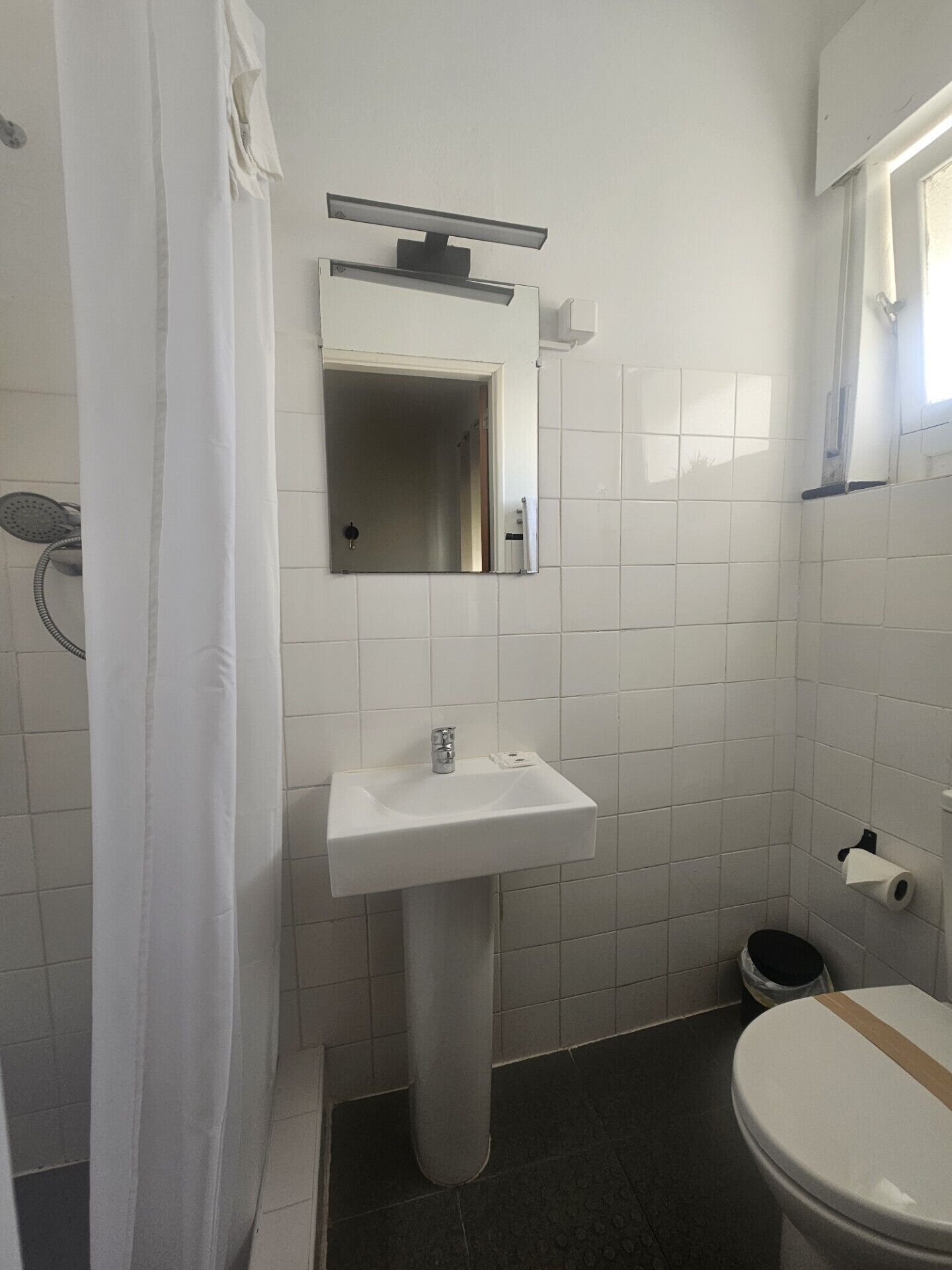 Une salle de bain avec un lavabo blanc, un miroir, un rideau de douche et des toilettes.