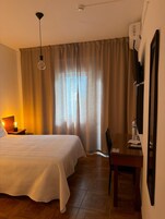 A hotel room with a bed, a desk, a chair, a lamp, a water bottle, and a television on the wall.