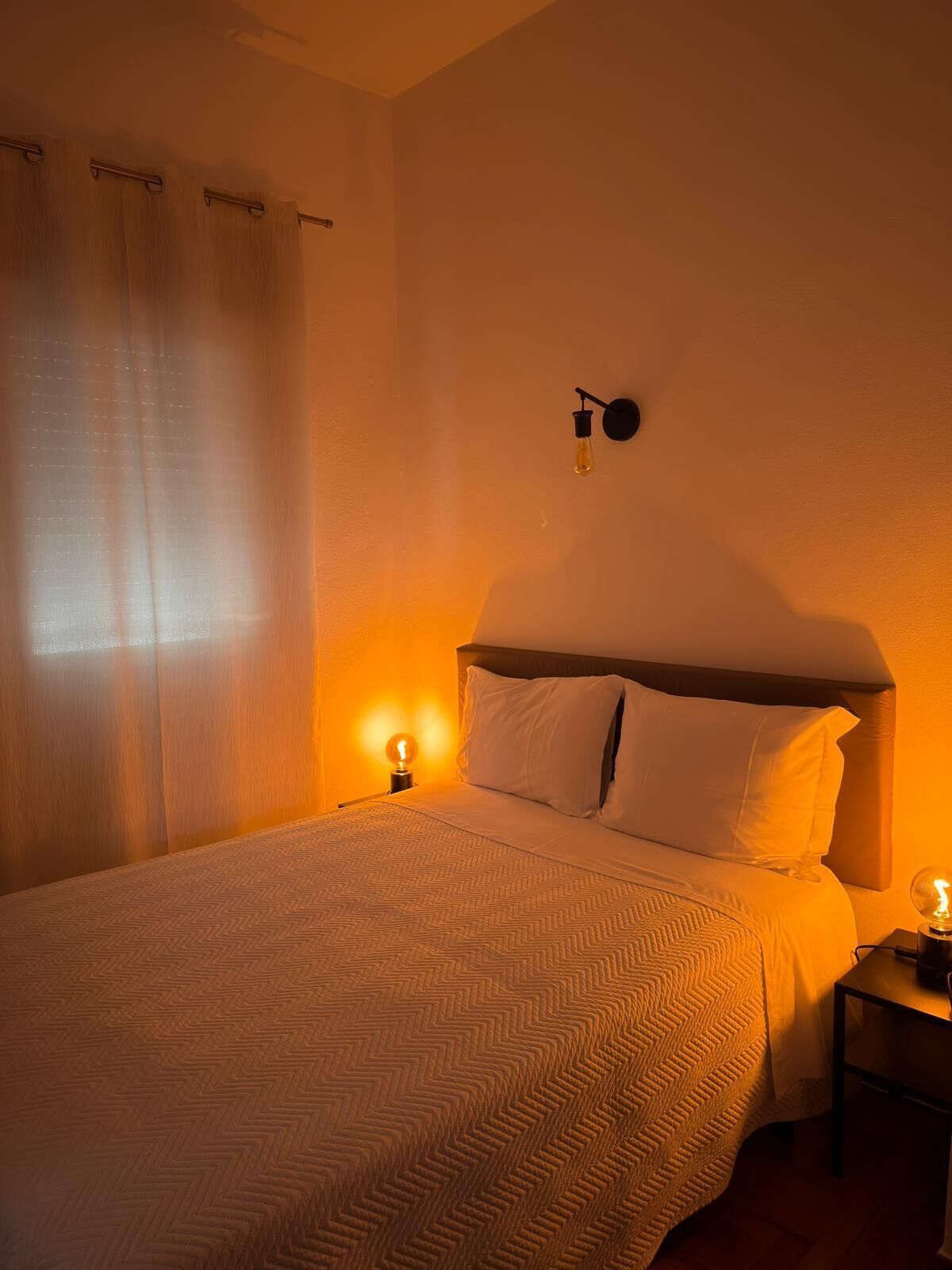 A hotel room with a large bed, a nightstand with a lamp, and a wall-mounted light fixture.