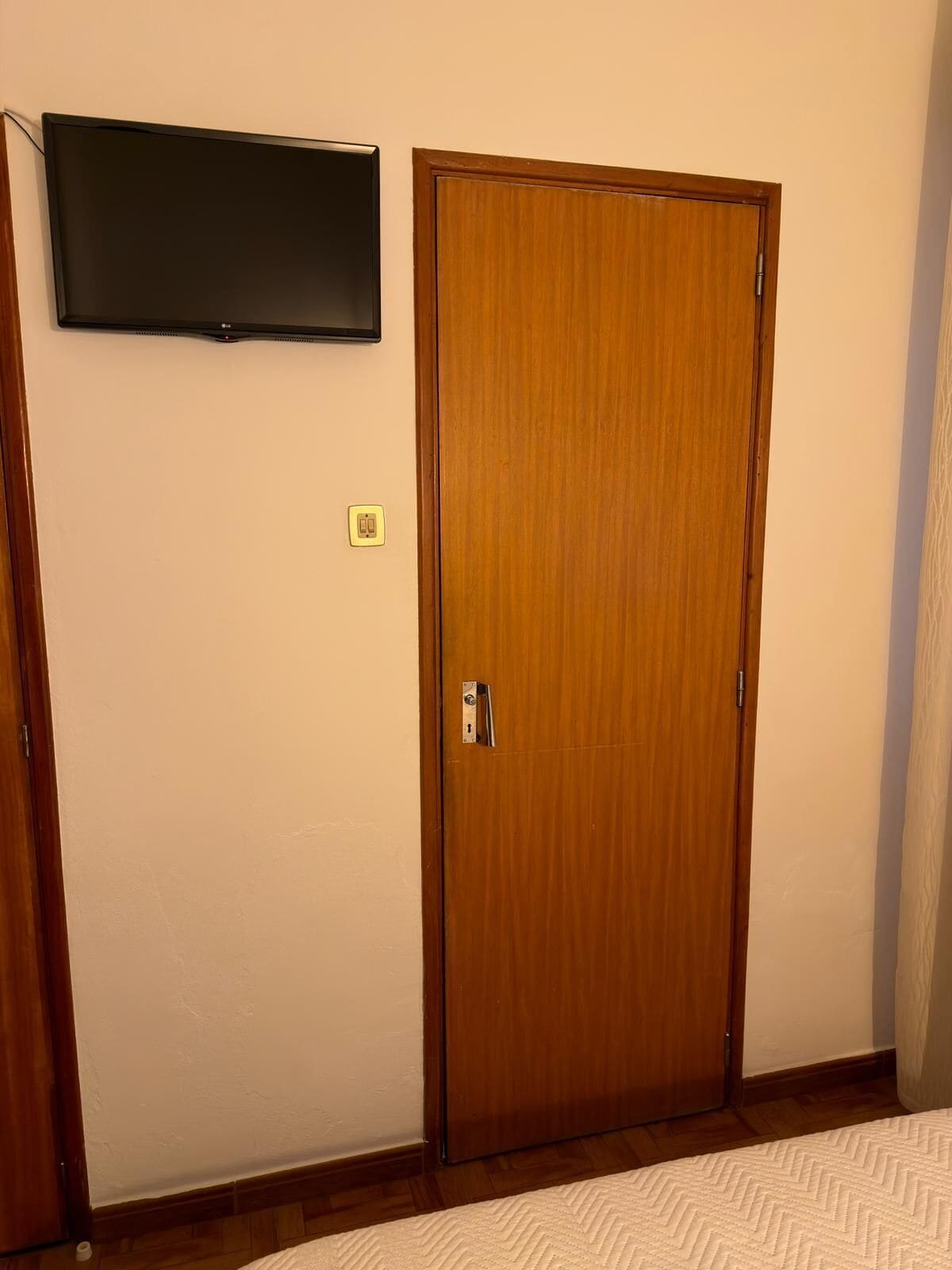 Una habitación con puerta de madera, un televisor de pantalla plana en la pared y un enchufe.