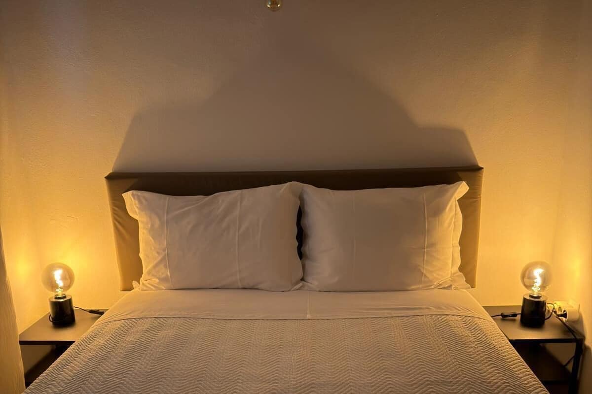 A neatly made bed with a patterned bedspread, two bedside lamps, and a wall-mounted light fixture.