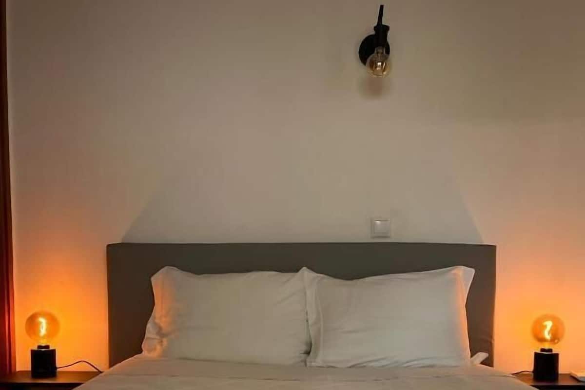 A neatly made bed with a white duvet, two bedside lamps, and a wall-mounted light fixture.