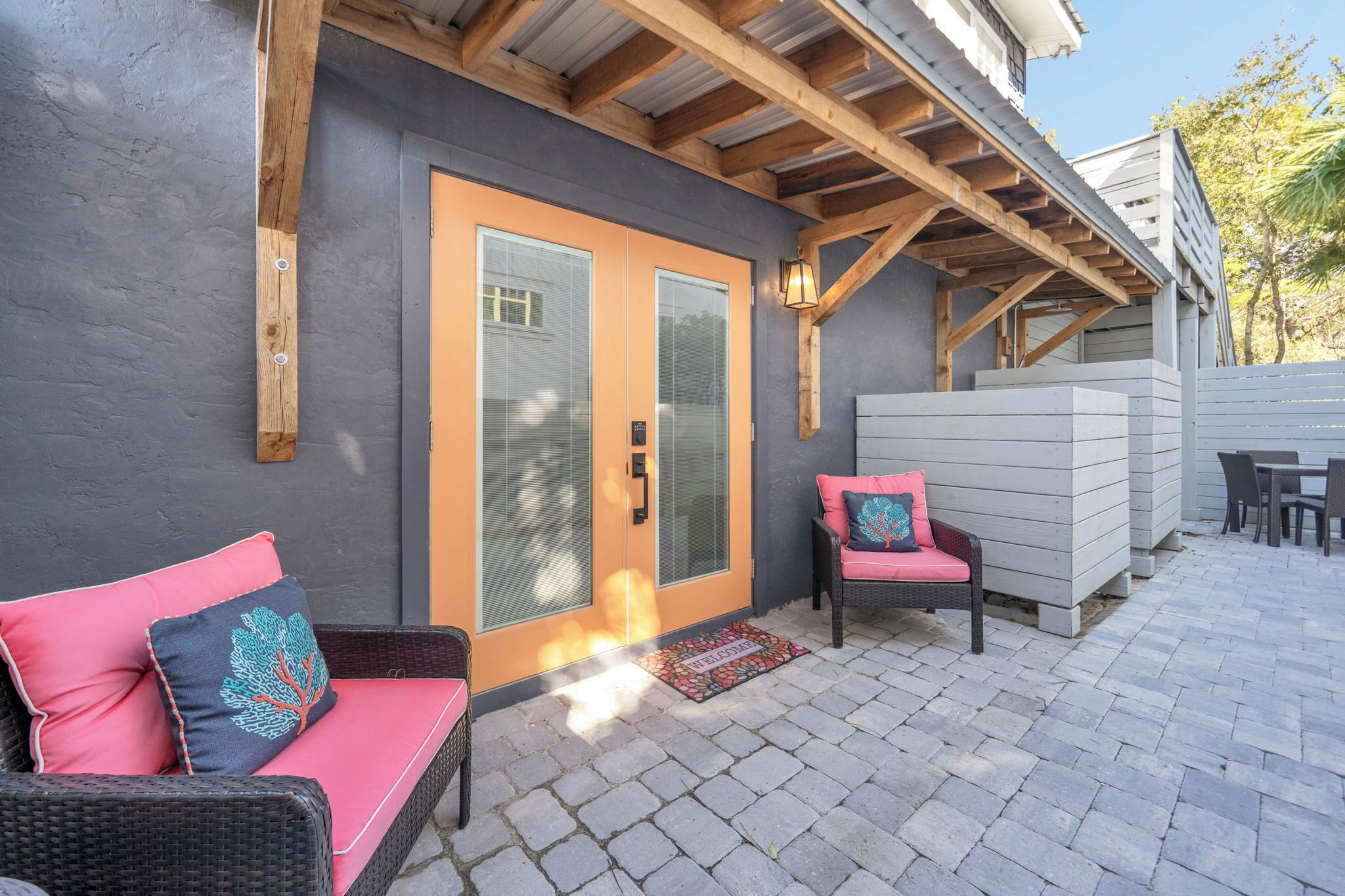 Un patio techado con mobiliario de mimbre, una puerta con paneles de vidrio y una estructura de techo de madera.