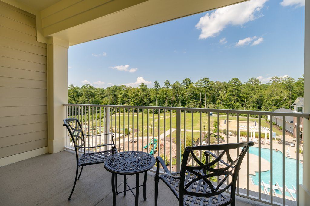 A balcony with two chairs and a table, overlooking a swimming pool and a green space.