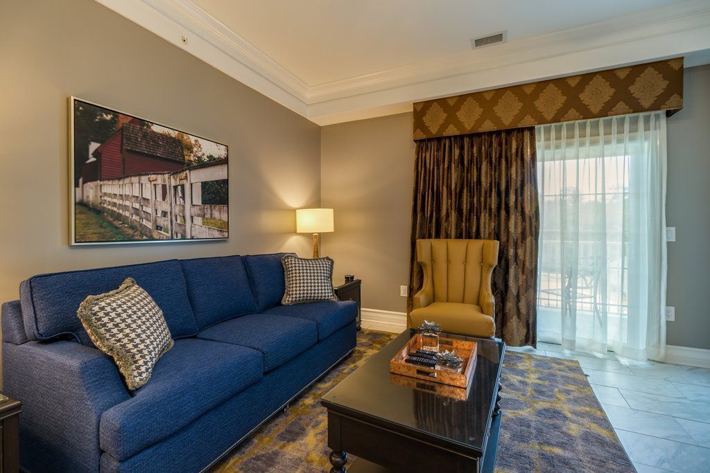 A living room with a blue sofa, a coffee table with decorative items, a lamp, and a large window with curtains.