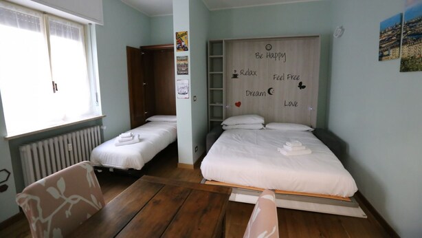 Quarto com duas camas de solteiro, uma mesa de madeira, uma cadeira, um radiador e uma janela com cortinas.