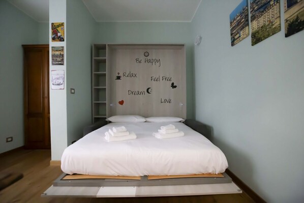 A neatly made bed with towels, a wall with motivational phrases, and a wooden door.