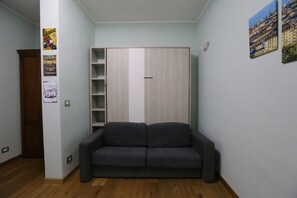 Een kamer met een grijze bank, een kledingkast en een deur.