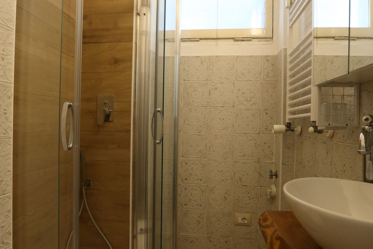 Un bagno con cabina doccia in vetro, lavandino bianco e mobile bagno in legno.