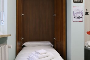 Een eenpersoonsbed met witte lakens en handdoeken, een houten deur en een radiator aan de linkerkant.