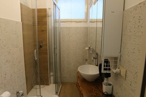 A bathroom with a glass-enclosed shower, a white sink, and a wooden vanity. - Casa Hexa – Smart studio with balcony, AC & free parking (Torino)