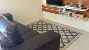 Una sala de estar moderna con un sofá de cuero, un televisor de pantalla plana montado en una pared de madera, un estante con objetos decorativos y una alfombra estampada.