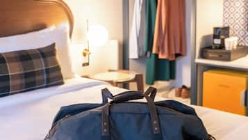 A hotel room with a bed, a bedside lamp, a wardrobe, and a desk with a lamp.