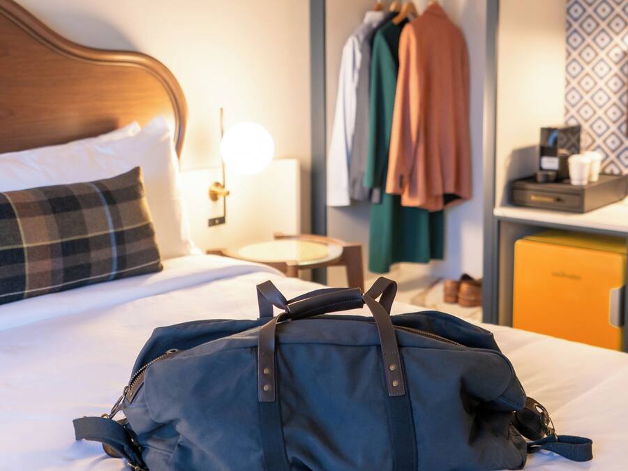 A hotel room with a bed, a bedside lamp, a wardrobe, and a desk with a lamp.