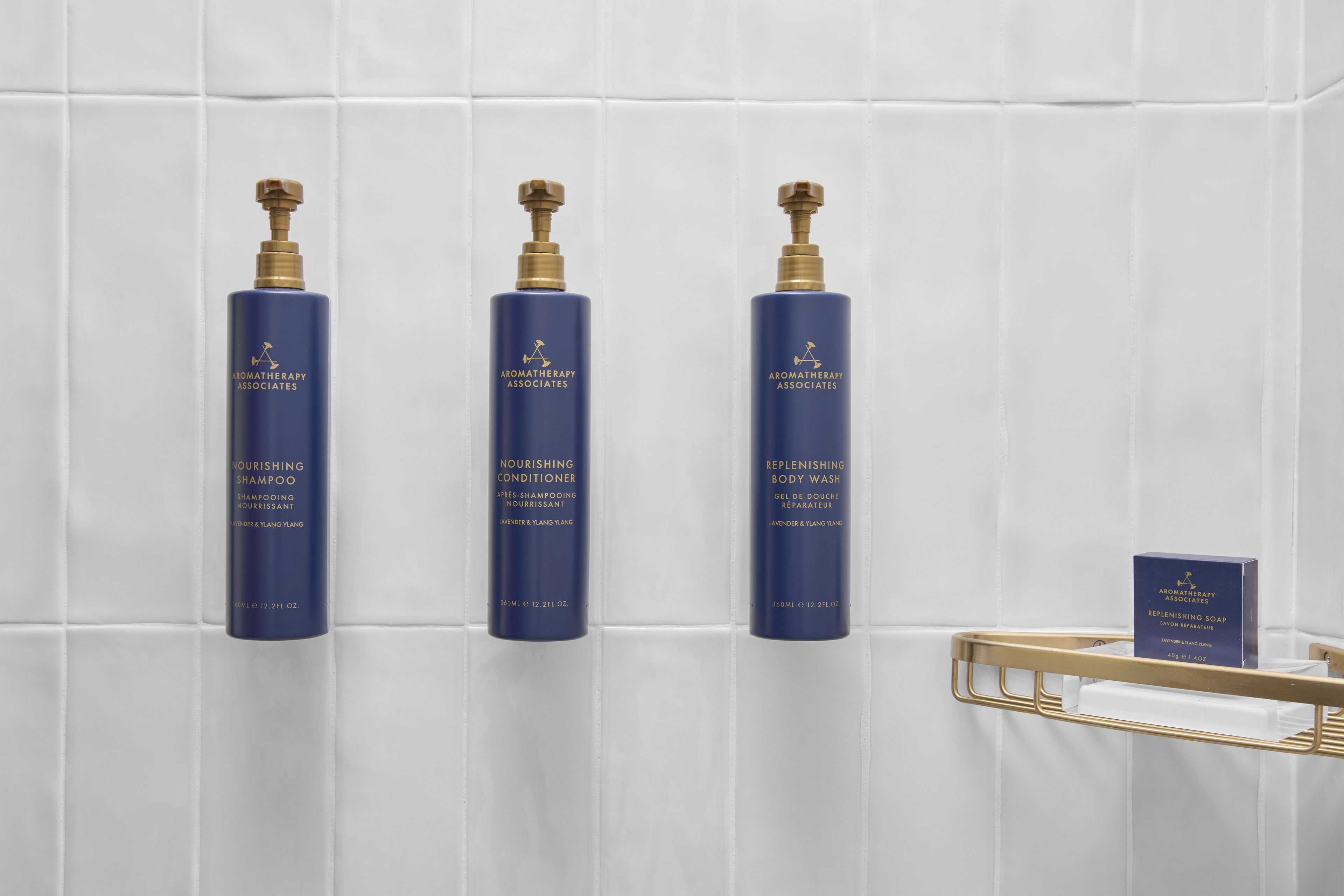 Three bottles of Aromatherapy Associates products on a white tiled wall.