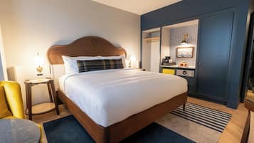 A hotel room with a bed, bedside table, lamp, chair, and a small table with a lamp.