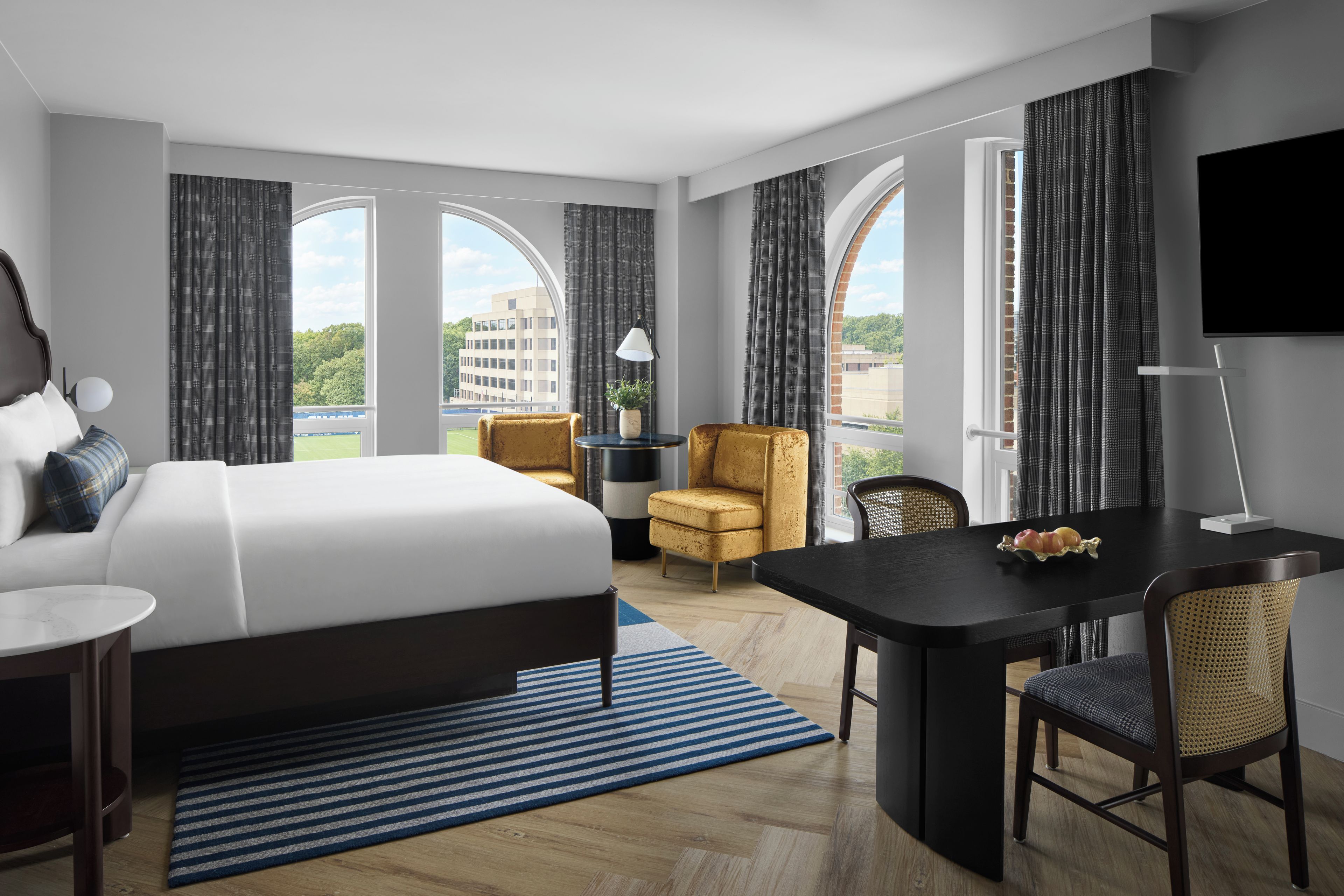 Habitación de hotel con una cama grande, un escritorio, una silla, un televisor y vistas a la ciudad.