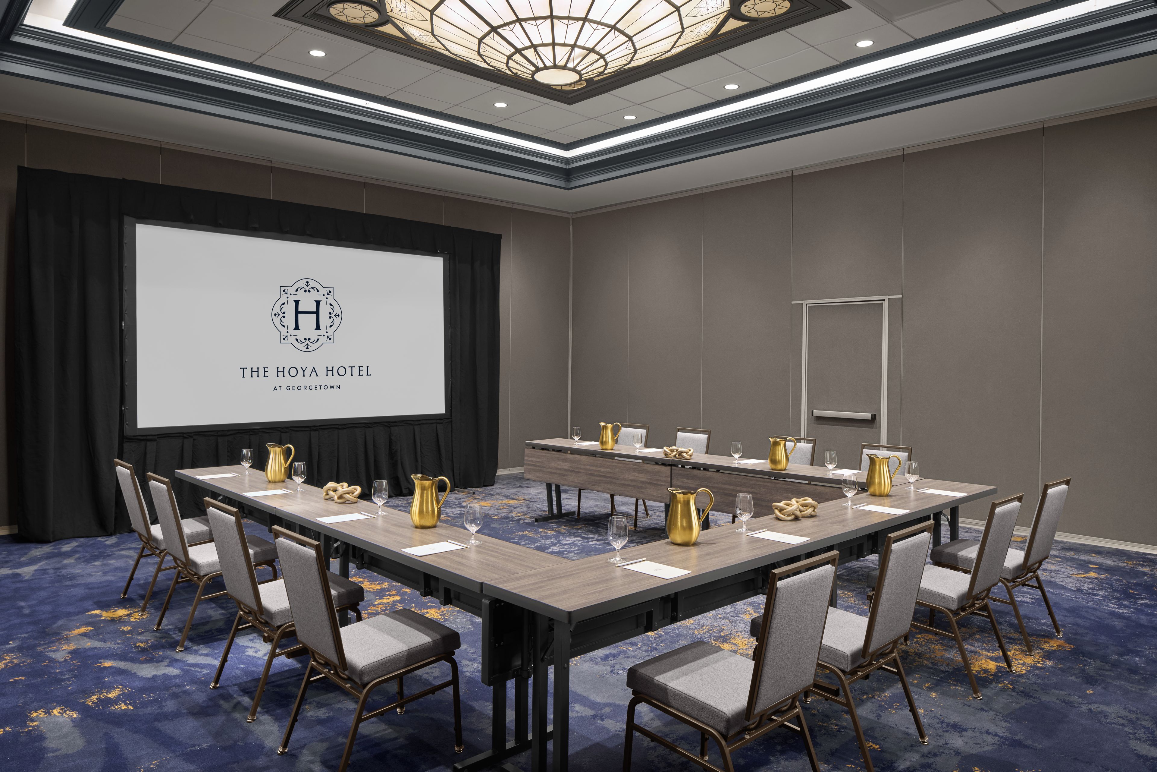 A conference room with a long table, chairs, a projector screen, and a logo on the screen.