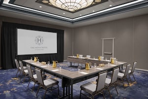 A conference room with a long table, chairs, a projector screen, and a logo on the screen.
