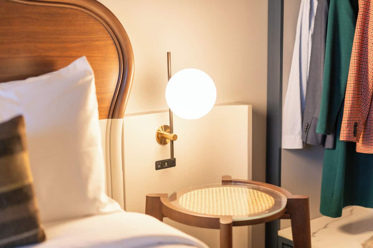A hotel room with a bed, a bedside table with a lamp, a chair, and a wall-mounted mirror.