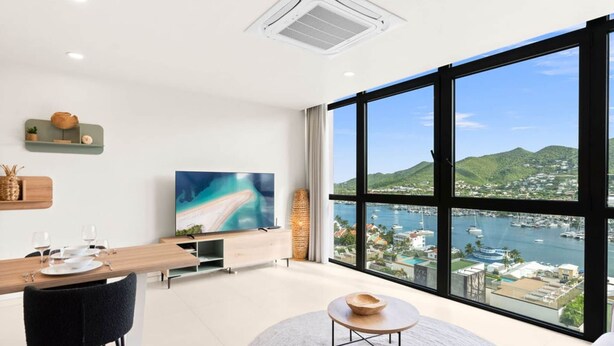 Un soggiorno moderno con un'ampia finestra, una TV a schermo piatto, un'area pranzo e vista su una cittadina costiera.