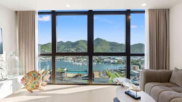 Un salon spacieux doté d’une grande fenêtre donnant sur un port et des collines.