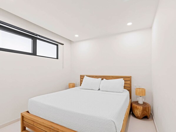 A modern bedroom with a wooden bed frame, white bedding, and a small wooden nightstand with a lamp.