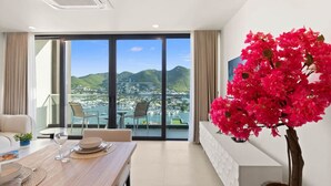 Ett modernt hotellrum med en matplats, ett stort fönster med utsikt över staden och bergen samt en krukväxt med en rosa bougainvillea.