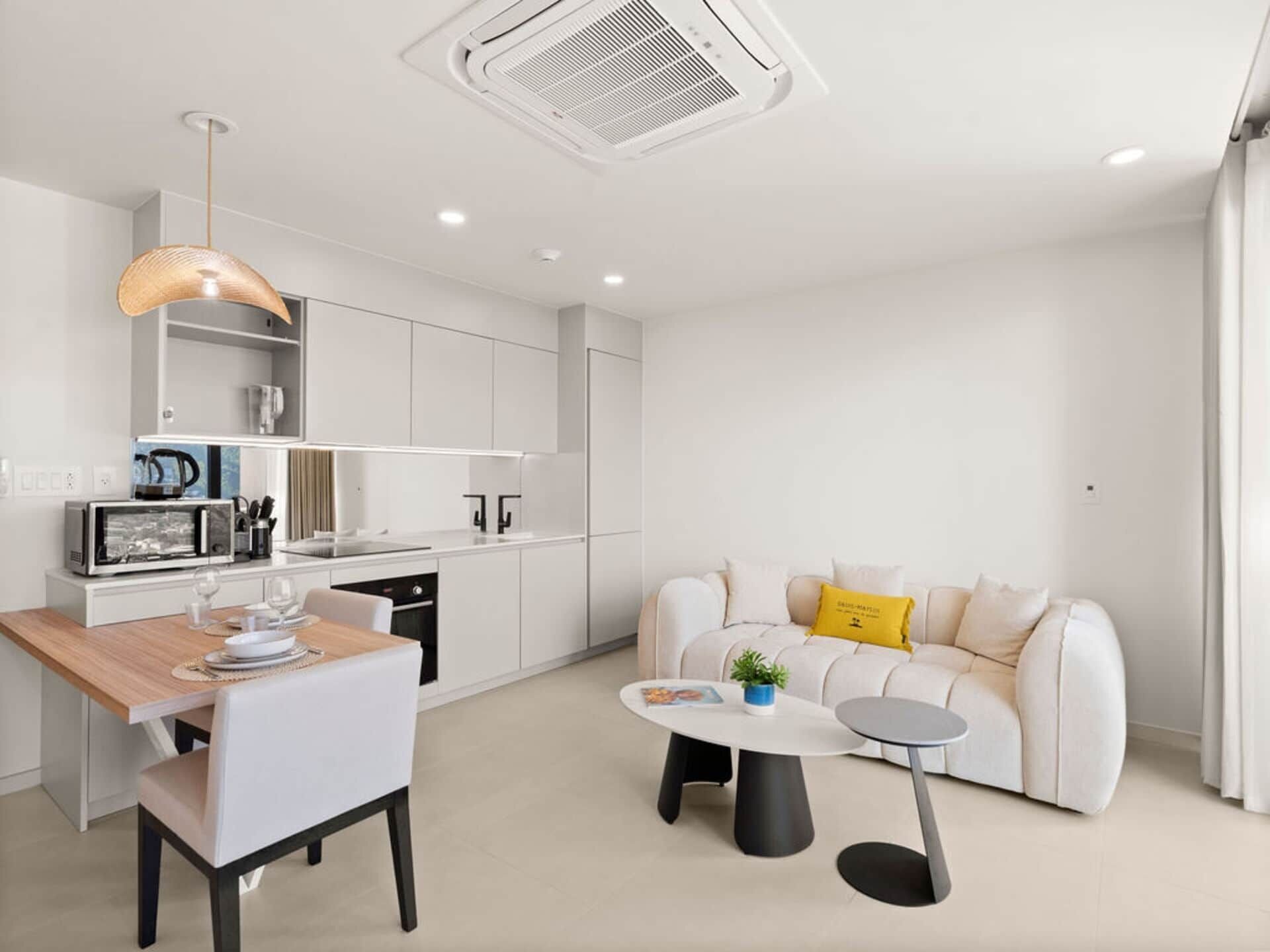 A modern kitchen with white cabinetry, a dining table with chairs, a round coffee table, and a sofa with cushions.