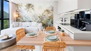 Une cuisine moderne avec un coin repas, comprenant un grand îlot central, des meubles blancs et une fresque murale aux motifs tropicaux.