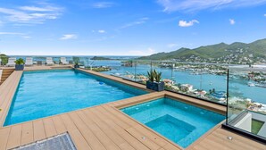 Une piscine sur le toit, dotée d’une terrasse en bois, de balustrades en verre et offrant une vue sur un port de plaisance et le paysage urbain.