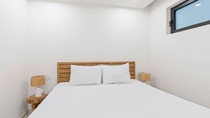 A neatly made bed with white linens, wooden headboard, and two bedside lamps on wooden nightstands. - D417 - One Bedroom Apartment with Lagoon View (Cole Bay)