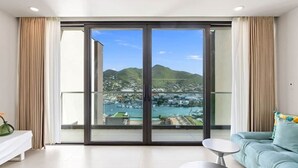 Un salón espacioso con un amplio ventanal corredera que da a un balcón con vistas a un puerto deportivo y colinas.