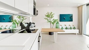 Una cocina moderna con armarios blancos, encimera de madera y una isla central. Hay dos plantas verdes en la isla y un cuadro en la pared.