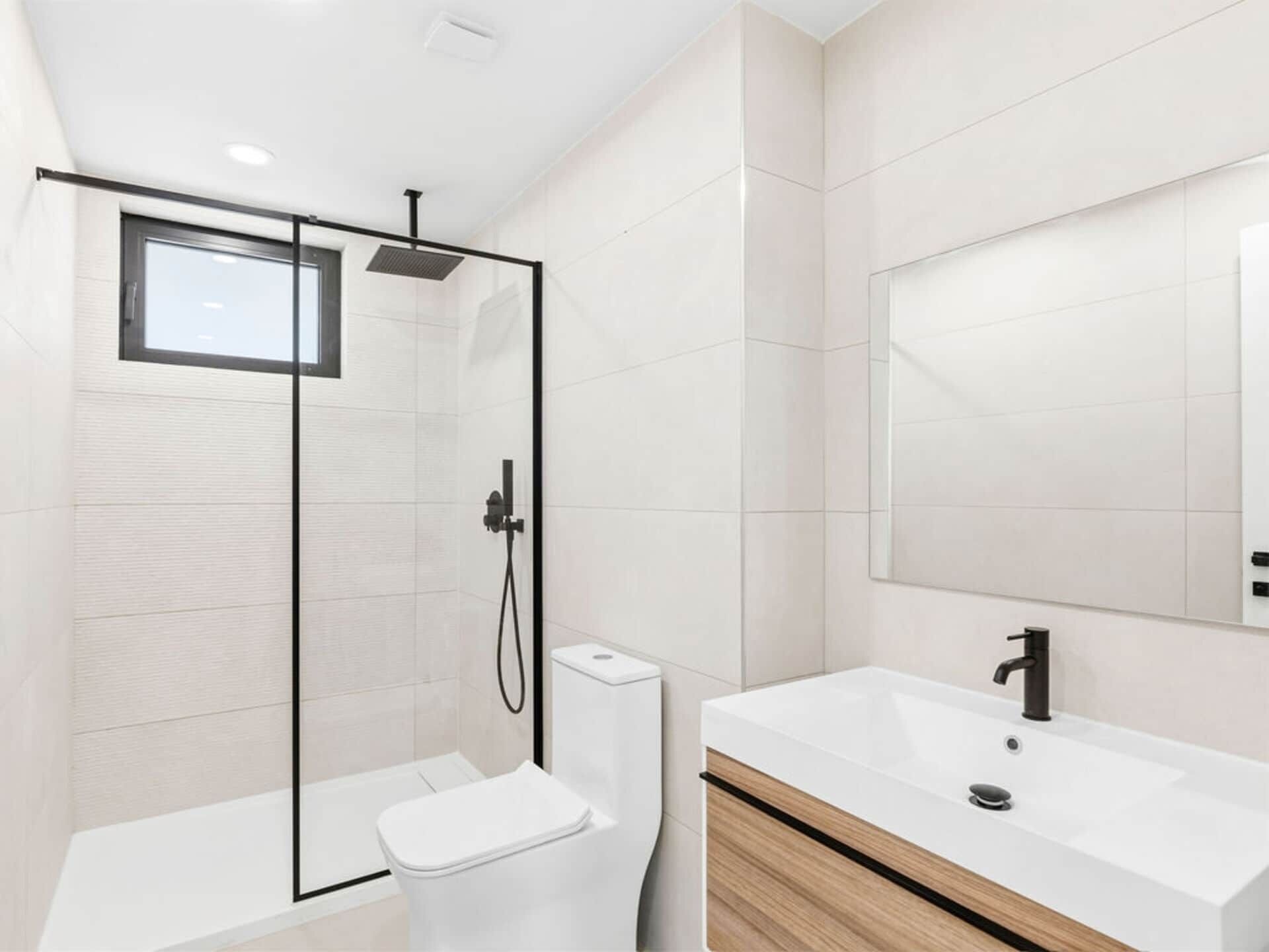 A modern bathroom with a glass-enclosed shower, a white toilet, and a vanity with a mirror.