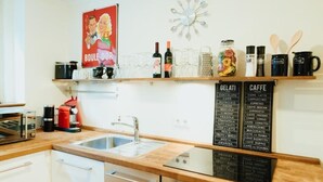 A modern kitchen with a wooden countertop, a built-in oven, a sink, and a coffee station with a menu board listing various coffee types. - Cozy 1-room apartment in central Hamburg Altona (Ottensen)